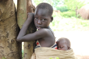Jepa, caries her baby sibling near their home in Nanda sub-county, Kiryandongo District. .  